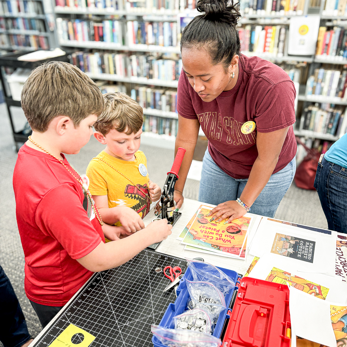 Noa helping two children with a craft project at a library playshop