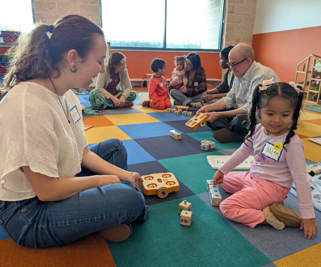 A facilitator and children playing with a programmable robot on the floor